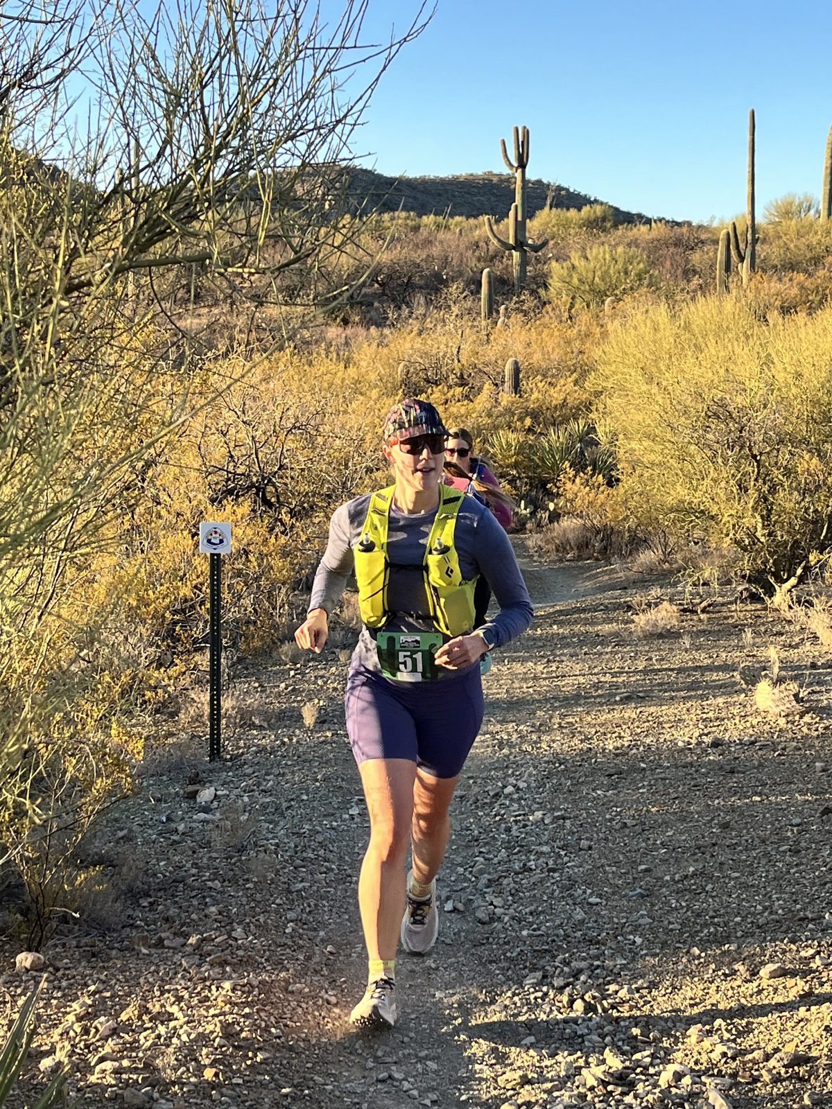 Runner in a yellow vest on the singletrack in morning light