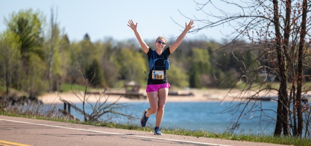 A runner celebrating with arms raised by the beach
