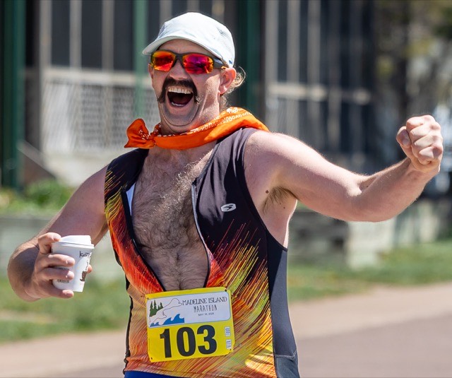 A finisher with a mustache and a big grin pumping his fist