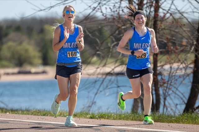 Two runners in Milers singlets smiling along the lake